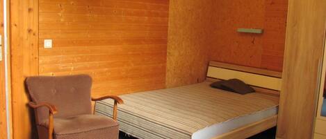 A small, cozy room with a single bed, a chair, and wooden walls.