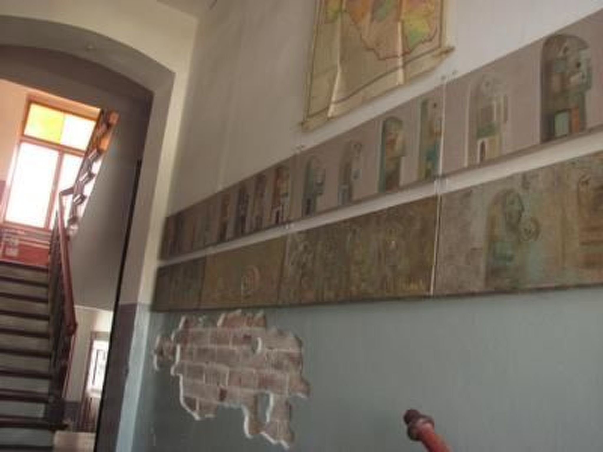 Una escalera con barandilla de madera y una pared decorada con varias obras de arte enmarcadas.