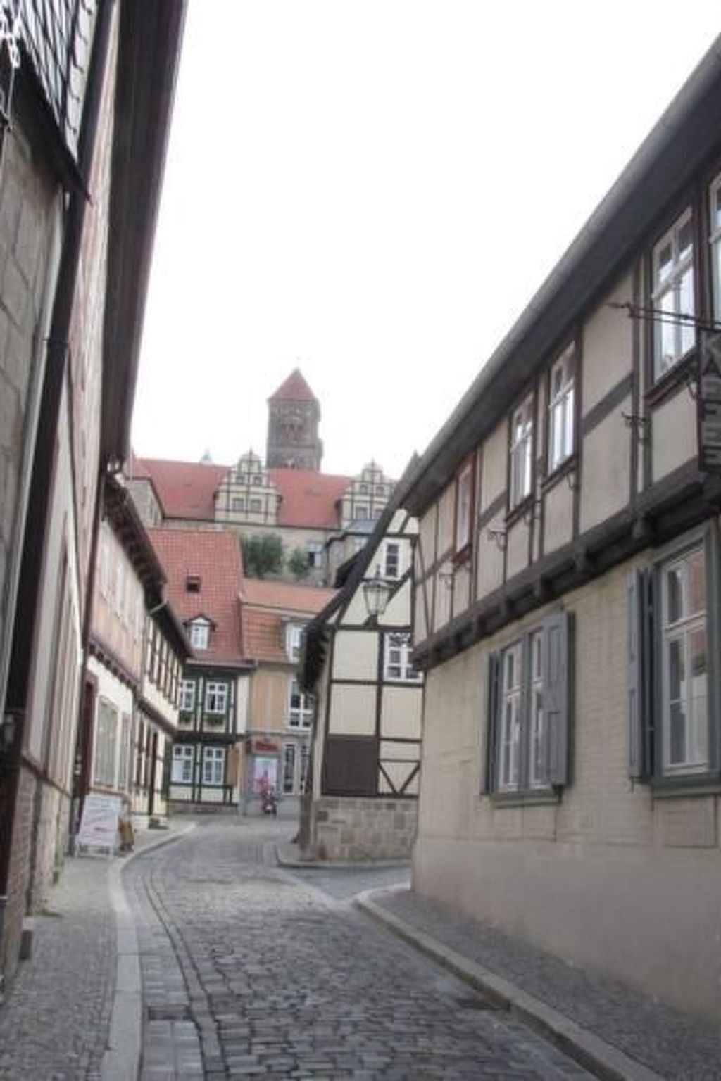 A narrow cobblestone street lined with traditional half-timbered buildings, leading to a tower in the distance.