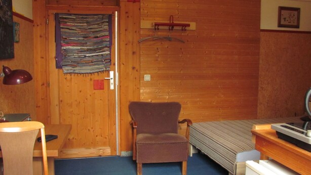 A small room with a wooden door, a chair, a desk, and a bed. - Kunst Asyl by Interhome (Quedlinburg)