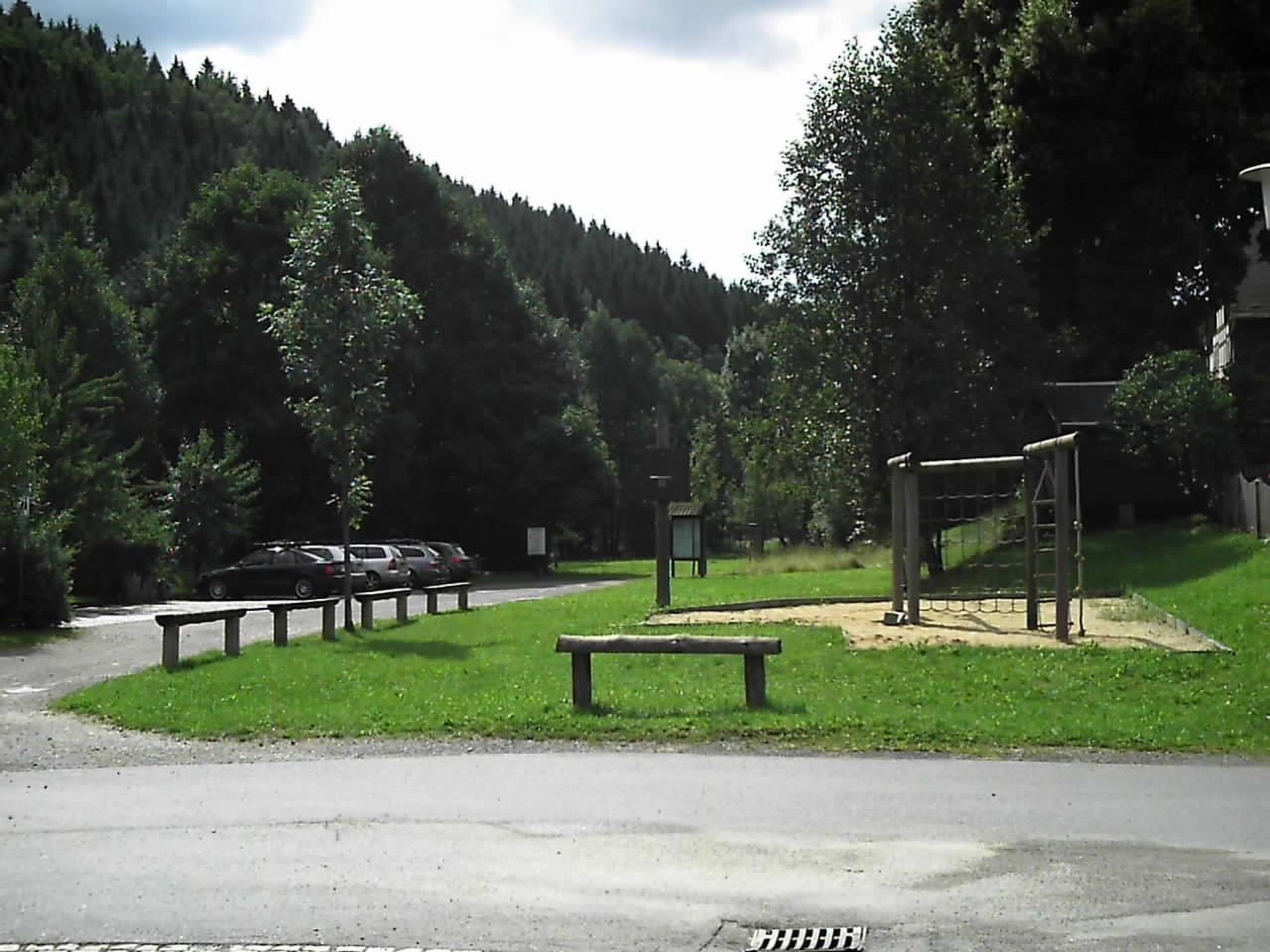 A parking area with cars, a picnic table, and a playground structure.