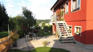 Ein rotes Haus mit einer Holzterrasse, einem kleinen Tisch und Stühlen im Freien sowie einer Treppe, die zu einem Balkon führt.
