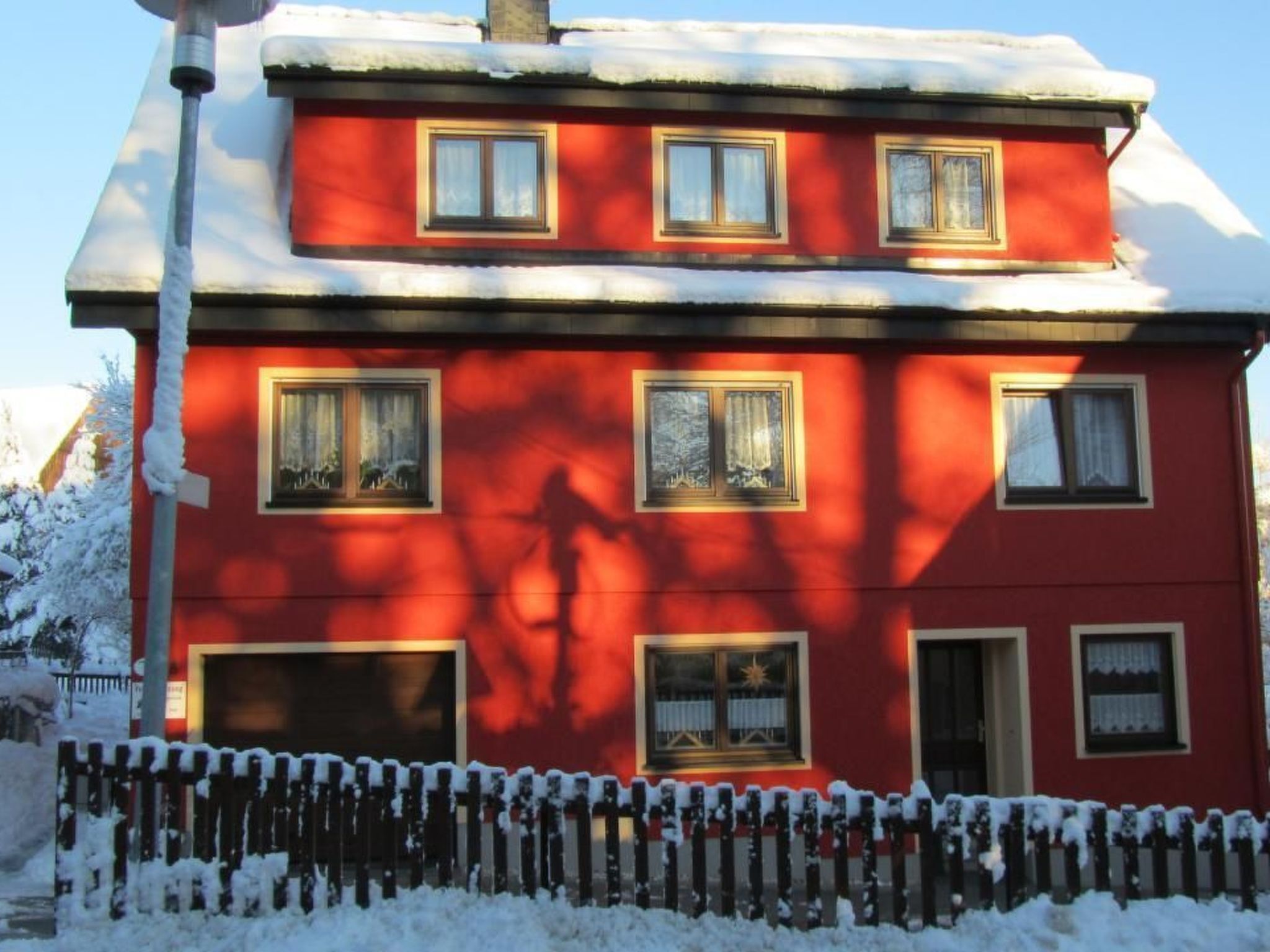 A red two-story house with multiple windows, a chimney, and a snow-covered roof.
