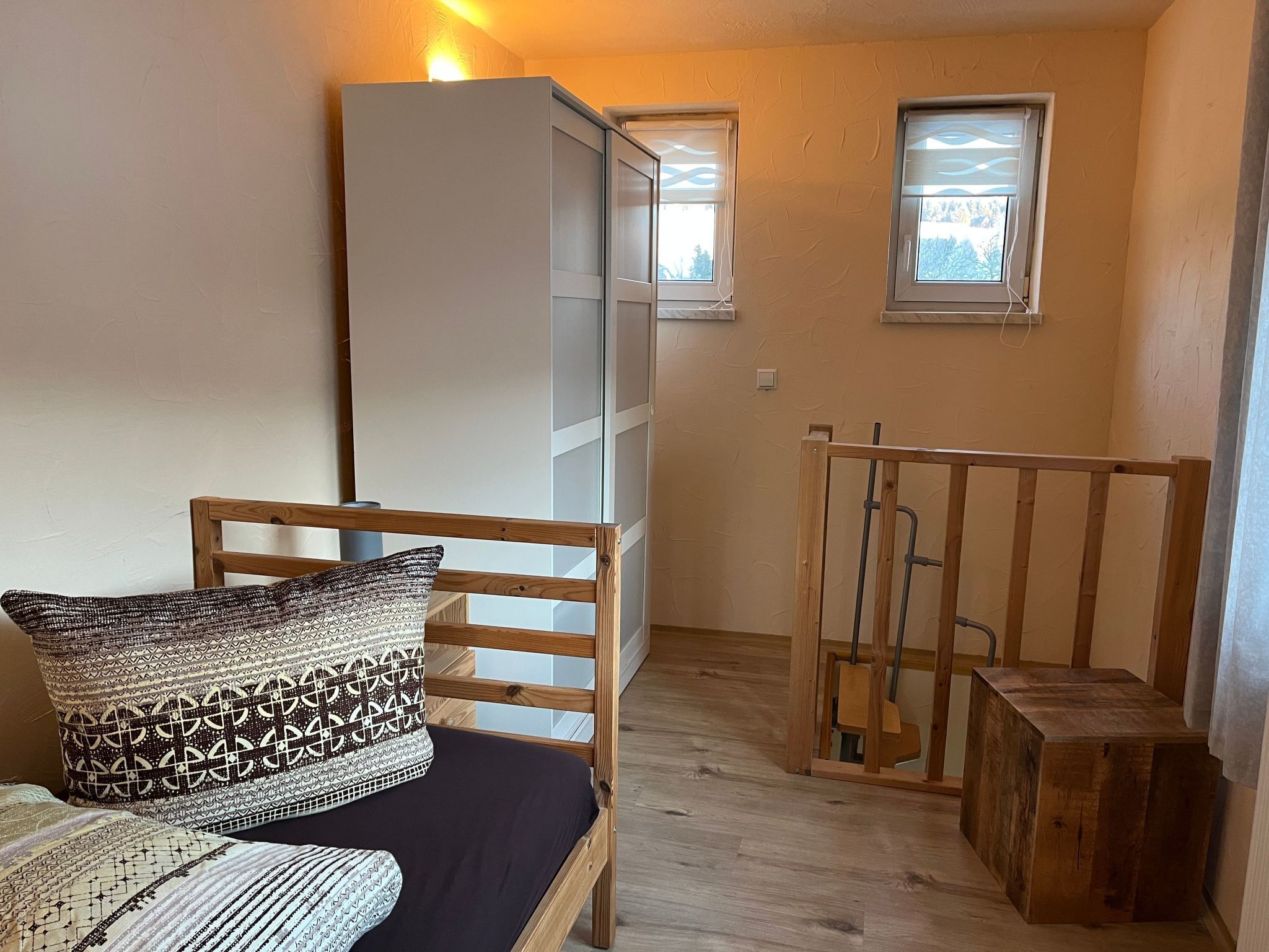 Ein kleiner, gemütlicher Raum mit einem Bett, einer hölzernen Bank und einem Fenster.