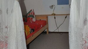 Een slaapkamer met een enkel bed, witte gordijnen, een muur met een schipdecoratie en een klein bureau met een lamp.