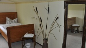 Een slaapkamer met een houten bed, een klein nachtkastje, een witte schaal en een vaas met hoge grassen.