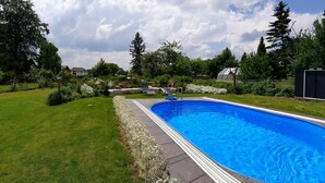 Una piscina rectangular con superficie de agua azul cristalina, rodeada por un césped cuidado y diversas plantas.
