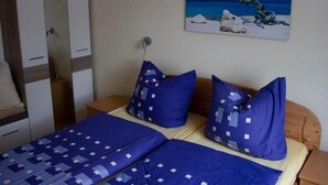 Un dormitorio con una cama, dos almohadas, una mesita de noche, un armario y un cuadro con una playa.