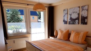 Ein Schlafzimmer mit Bett, Fenster, Heizkörper und Bildern an der Wand.