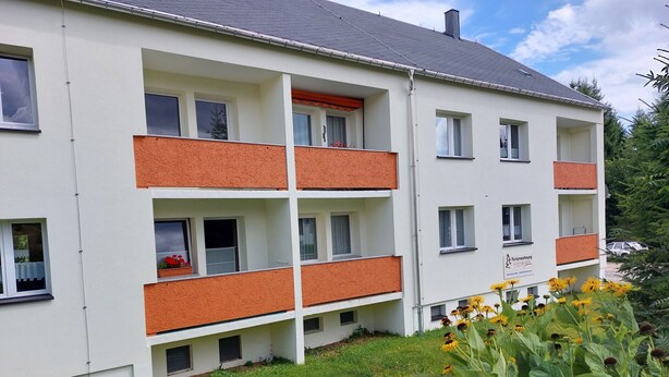 Ein mehrstöckiges Gebäude mit Balkonen, einer Rasenfläche und Blumen.