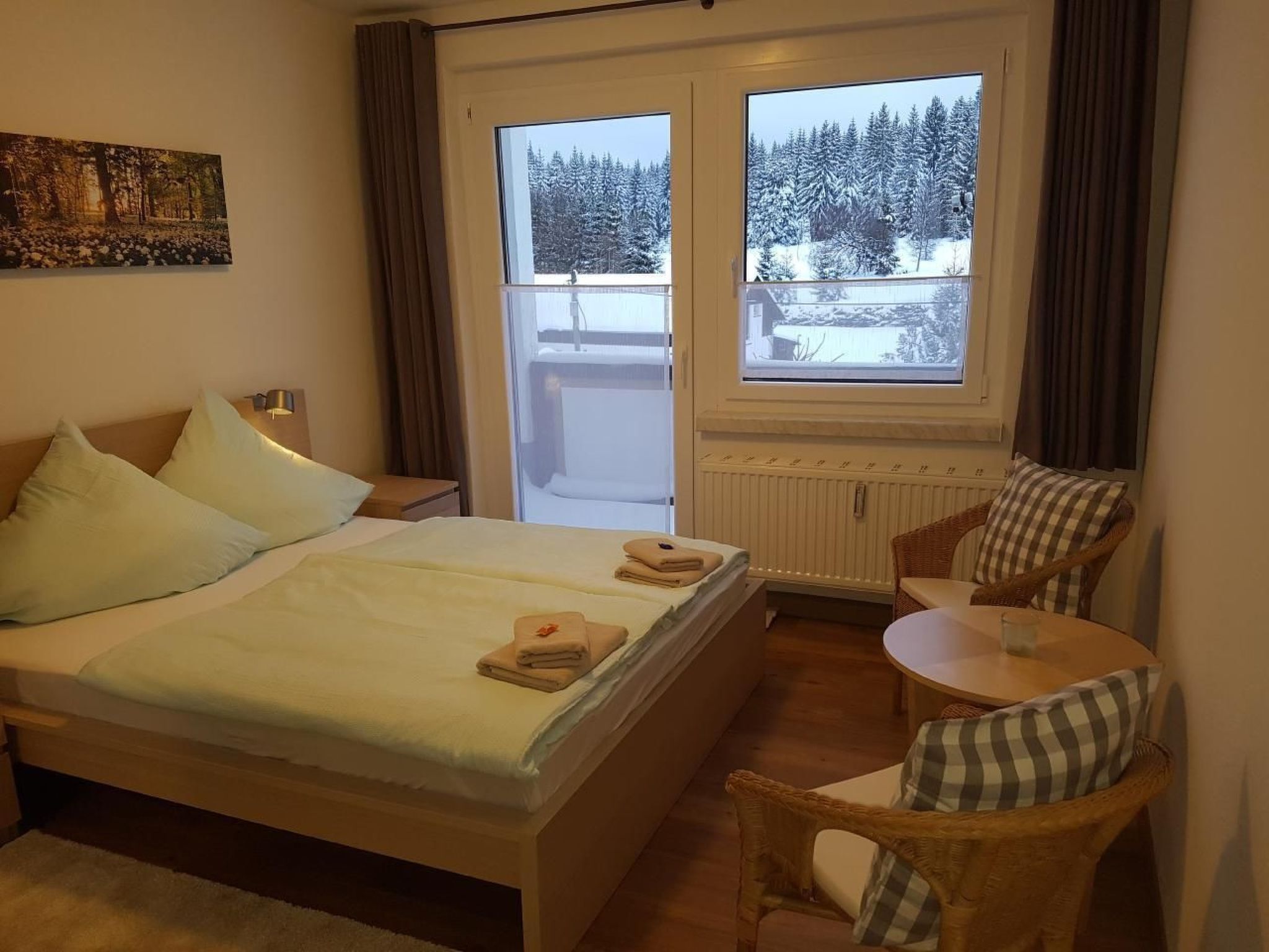 A hotel room with a bed, a chair, a small table, and a window with a view of snow-covered trees.
