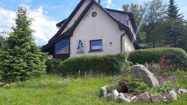 Un bâtiment à deux étages, doté d’un toit en pente, d’une cheminée bien visible et d’une petite fenêtre sur laquelle est inscrit le chiffre « 15 ».