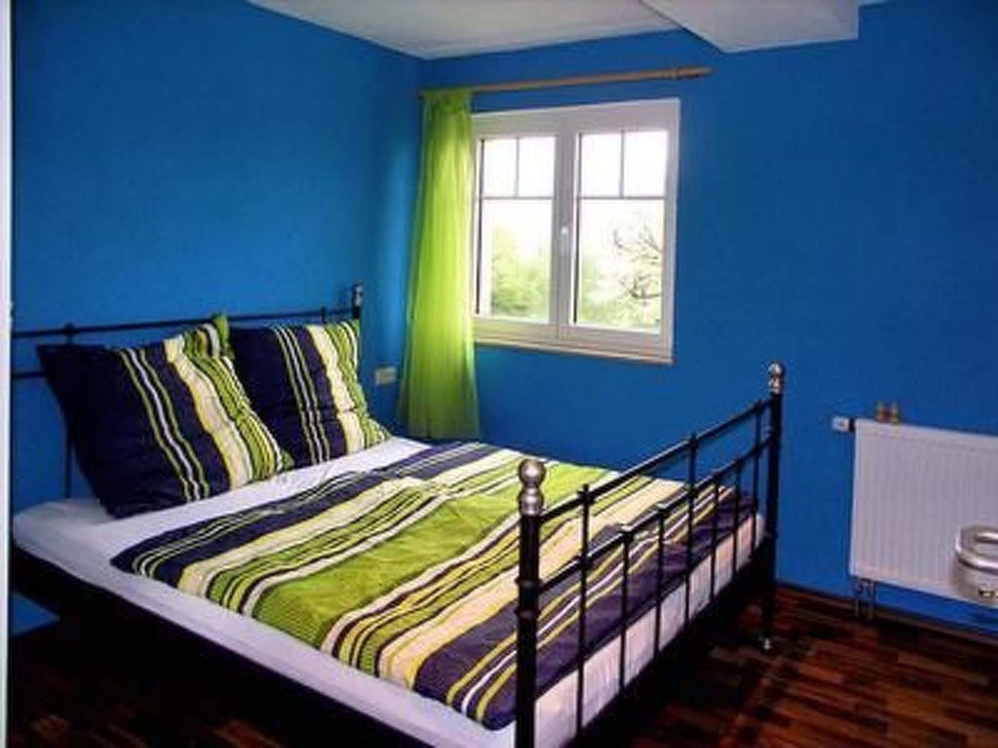 A bedroom with a bed, a window with a green curtain, and a radiator.