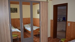 Une chambre avec un placard, deux lits, un petit tabouret et un coin cuisine.