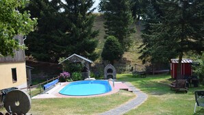 Un jardin avec une piscine, une terrasse en bois, une cheminée en pierre et un petit abri de jardin.