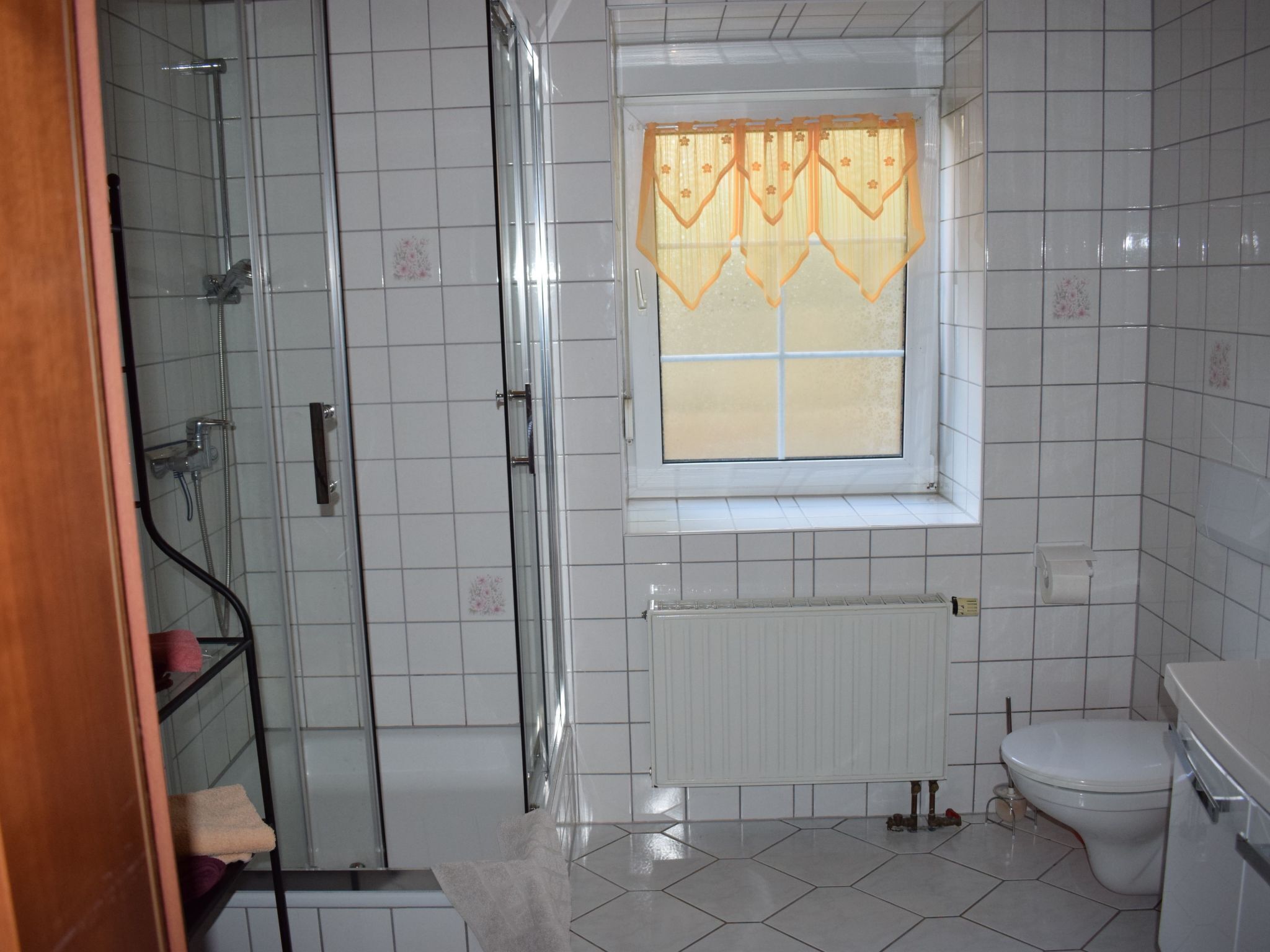 Ein Badezimmer mit Duschkabine, Toilette und einem Fenster mit dekorativer Vorhang.