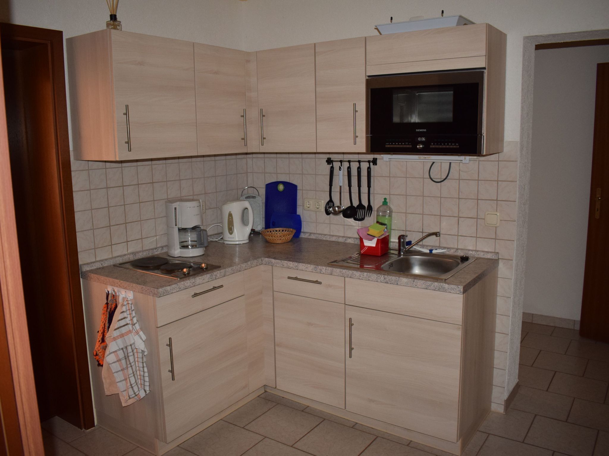 A compact kitchen with light wood cabinets, a built-in microwave, a coffee maker, and a sink.