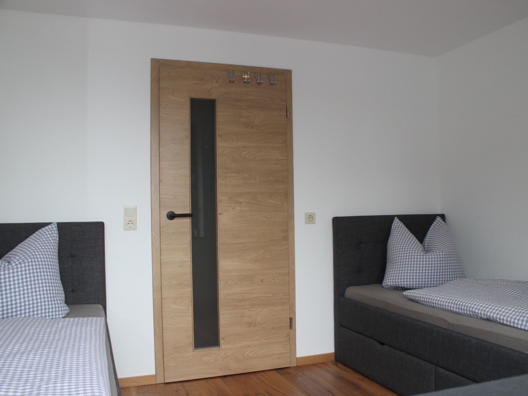 Ein Zimmer mit zwei Betten, einer Holztür mit vertikalem Griff und einem kleinen Fenster.