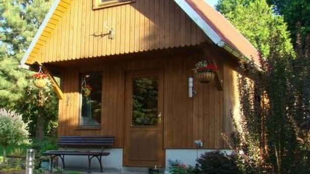 Une cabane en bois avec un toit en pente, un banc à l’extérieur et un petit espace aménagé en jardin.