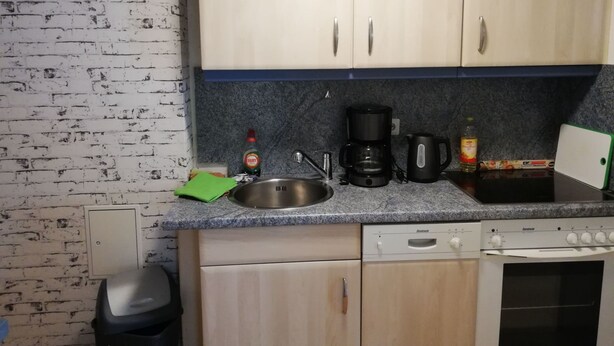 Une cuisine compacte dotée d’un plan de travail en granit, d’une machine à café, d’une bouilloire et d’un lave-vaisselle.