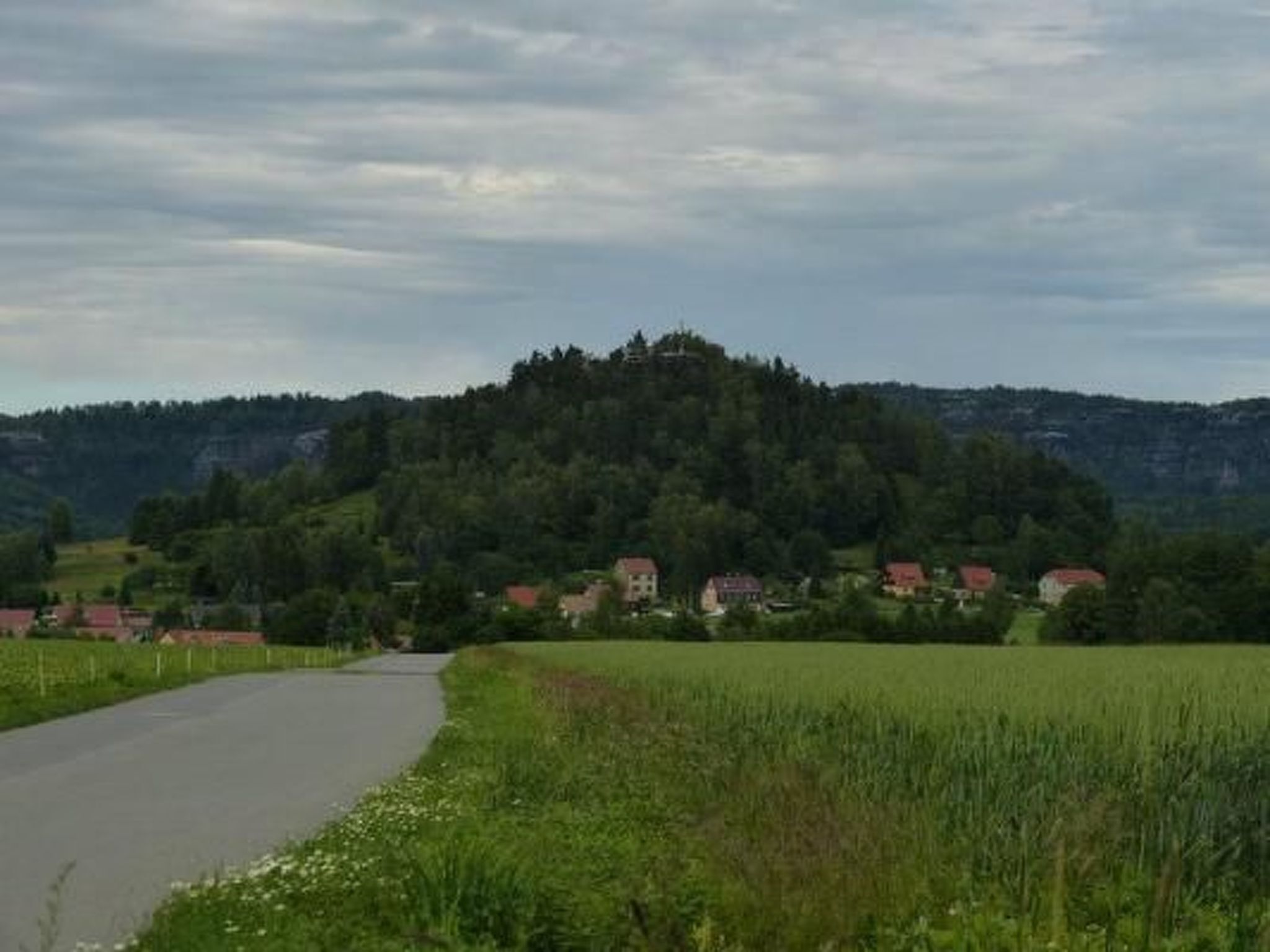 A rural road curving through a green landscape with houses on the hillside.