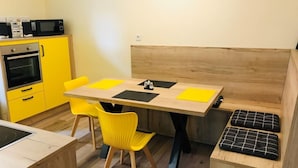 Una cucina compatta con mobili gialli, un forno a microonde e un forno. È presente una panca di legno con cuscini e un tavolino con sottopiatti gialli.