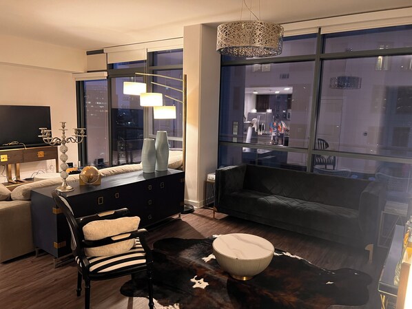 A modern living room with a sofa, a coffee table, a TV, and a dining area with a chandelier.