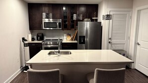 Une cuisine moderne avec des meubles en bois foncé, des appareils électroménagers en acier inoxydable, un îlot central doté d’un évier et deux chaises rembourrées.