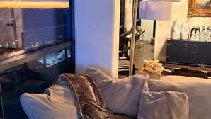 Un salon moderne avec un canapé, une couverture, une lampe et une vue sur le paysage urbain grâce à de grandes fenêtres.