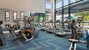 Une salle de sport équipée de tapis de course, de vélos elliptiques et de vélos d’appartement, disposés en rangées.