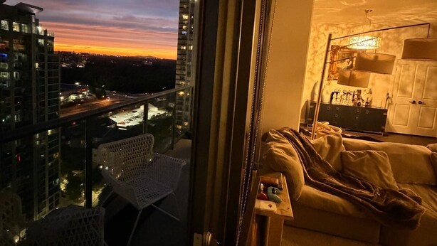 Un balcon donnant sur une vue panoramique de la ville au crépuscule, une chaise blanche et un canapé avec une couverture.