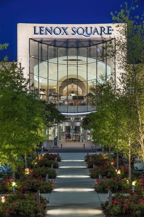 A modern Lenox Square building with a glass facade, a central entrance, and a landscaped walkway with flowering plants.