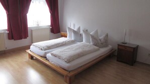 A double bed with white bedding in a room with wooden flooring and a window with red curtains. - Blaues Haus by Interhome (Meißen)