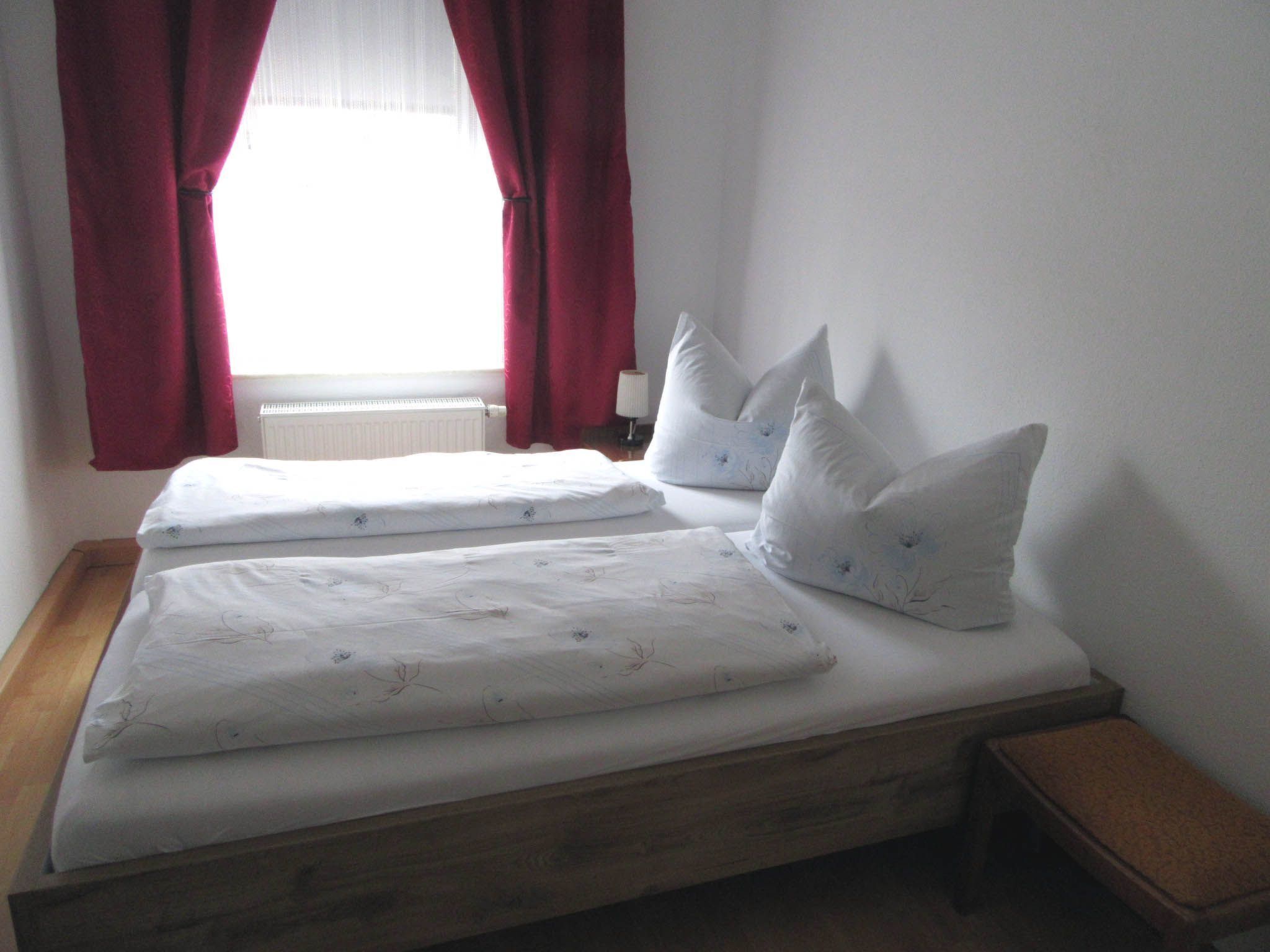 Ein Doppelbett mit weißer Bettwäsche und floralen Mustern, ein hölzernes Kopfende und zwei Kissen mit Blumenmotiv.