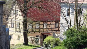 Uma rua estreita com casas tradicionais em estilo de enxaimel, um muro de pedra e uma caixa de correio.