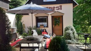 Een gezellig buiten zitgedeelte met een tafel en stoelen, een grote parasol, en een gebouw met een bord waarop 