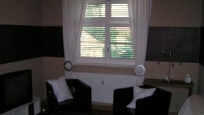 Habitació d'hotel amb llit, escriptori, cadira, televisió i finestra amb cortines.