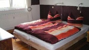 Un llit amb un llençol estampat i almoines, una finestra amb cortines i un radiador.