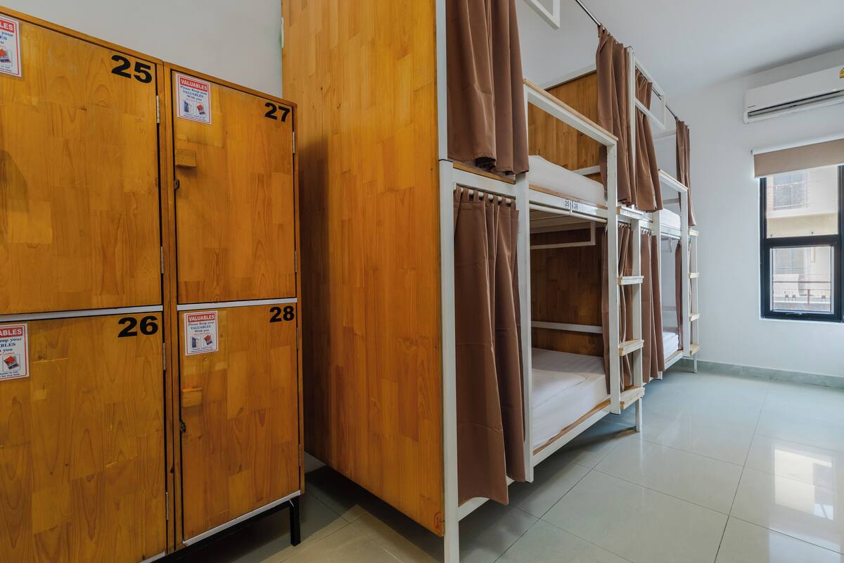 A dormitory room with bunk beds, wooden lockers numbered 25 to 28, and a window providing natural light.