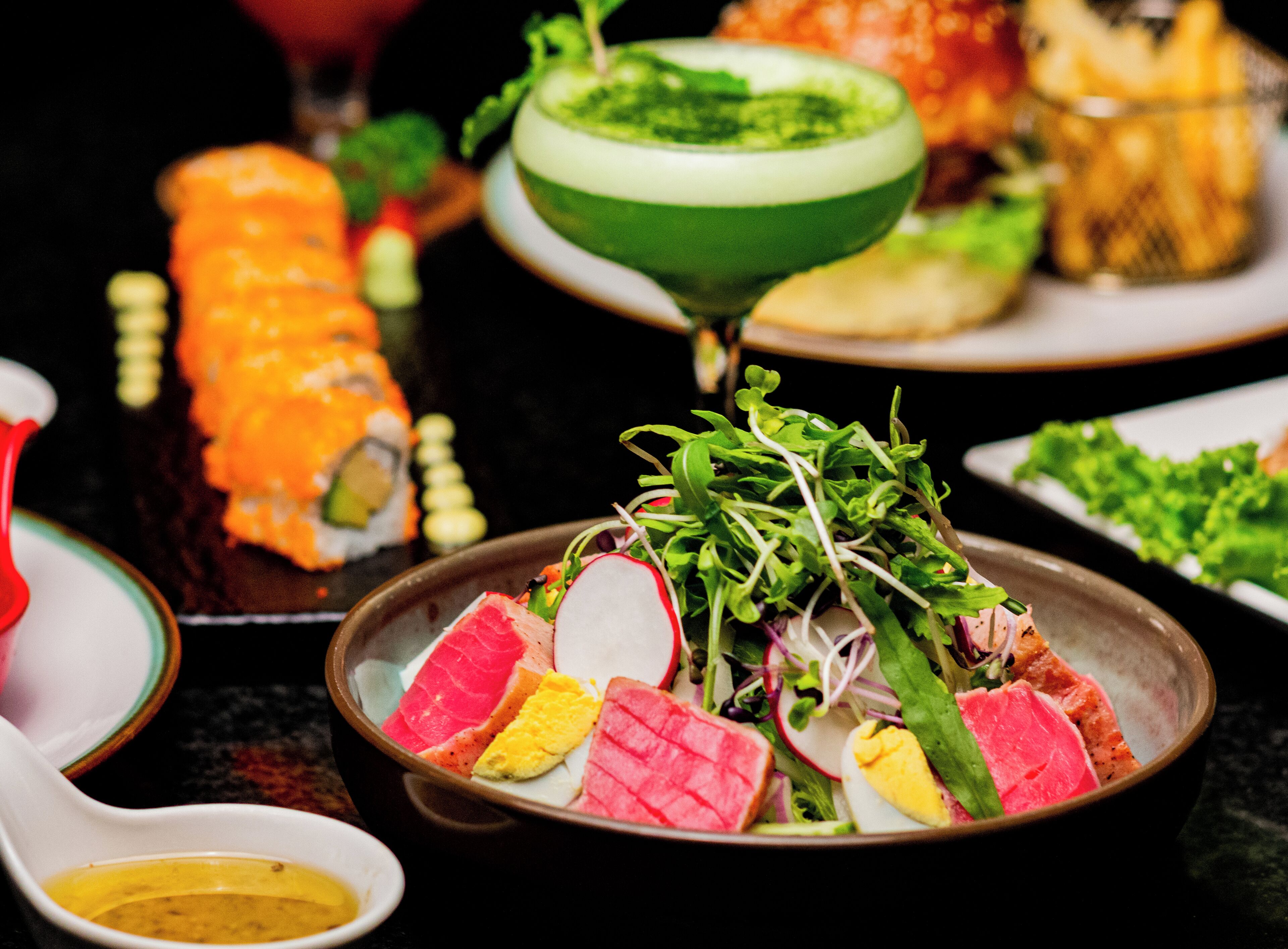 Variedad de platos, incluyendo sushi, un tazón de ensalada y un cóctel verde.