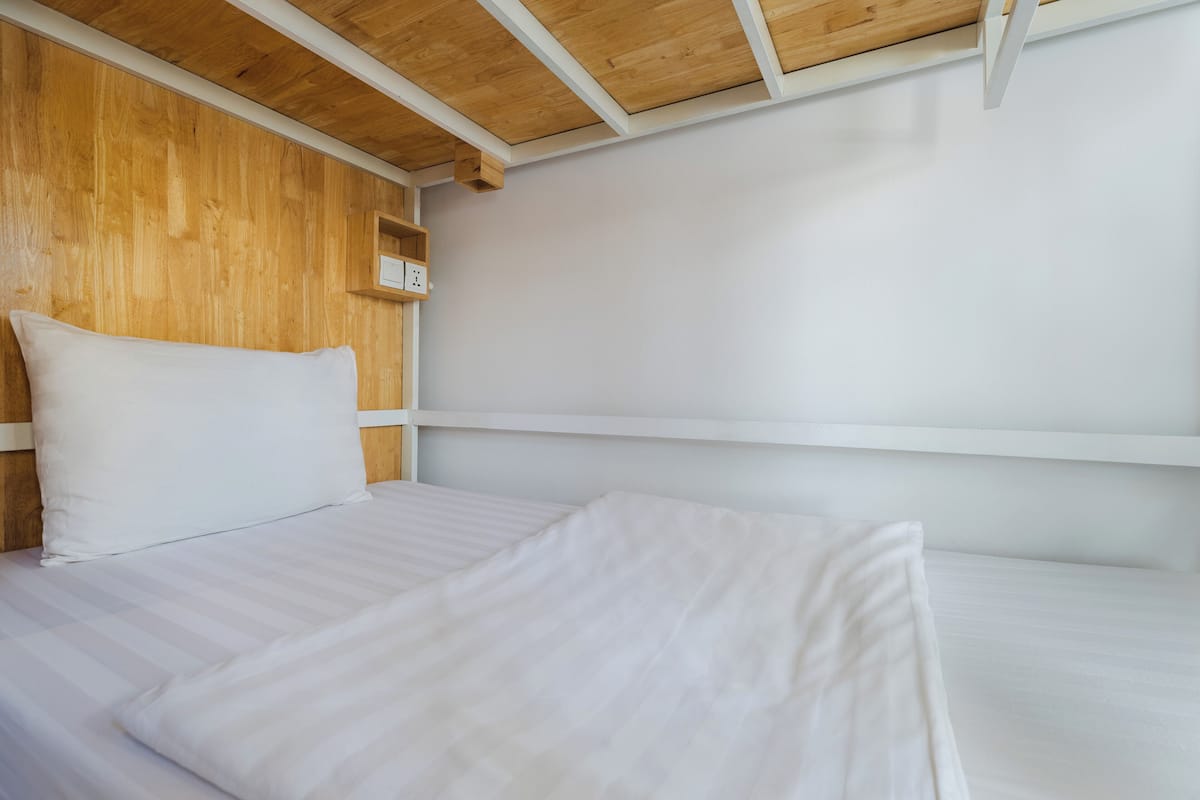 A clean, minimalist room with a wooden headboard, white bedding, and a white wall.