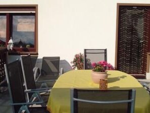 Un coin repas avec une table recouverte d’une nappe jaune, entourée de chaises. On peut voir une plante en pot sur la table.