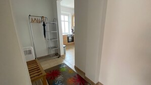 Un couloir avec un présentoir en métal, un banc en bois et un tapis coloré.