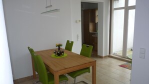 Un coin repas avec une table en bois, des chaises vertes et un vase rempli de fleurs.