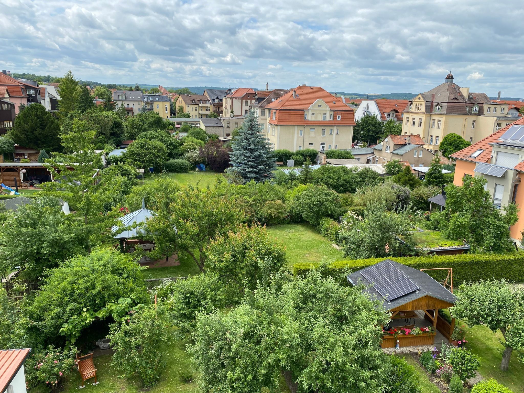 Un área residencial con casas y zonas verdes, incluyendo un árbol grande y jardines bien cuidados.