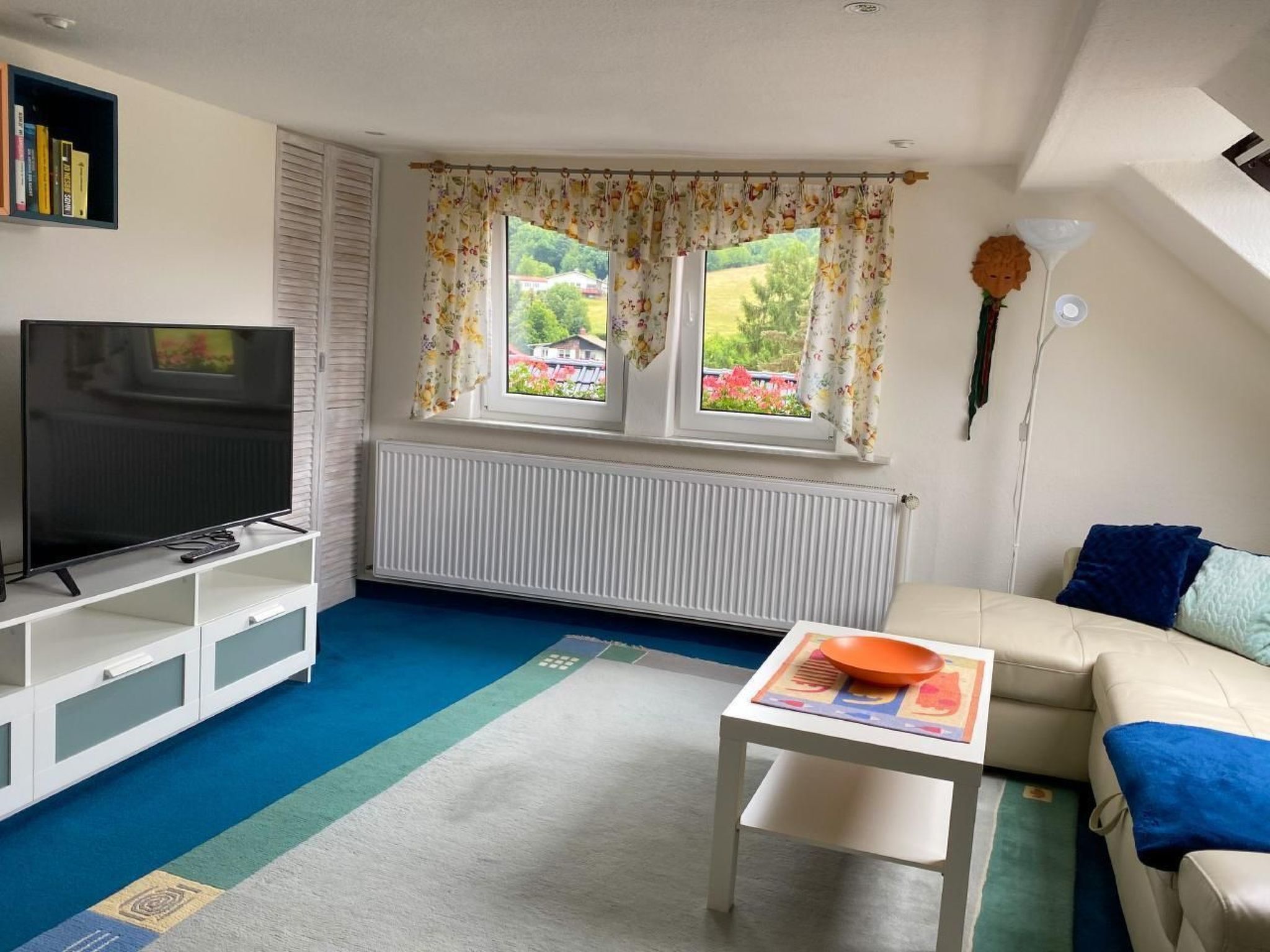 A living room with a TV, a sofa, a small table, and a window with curtains.