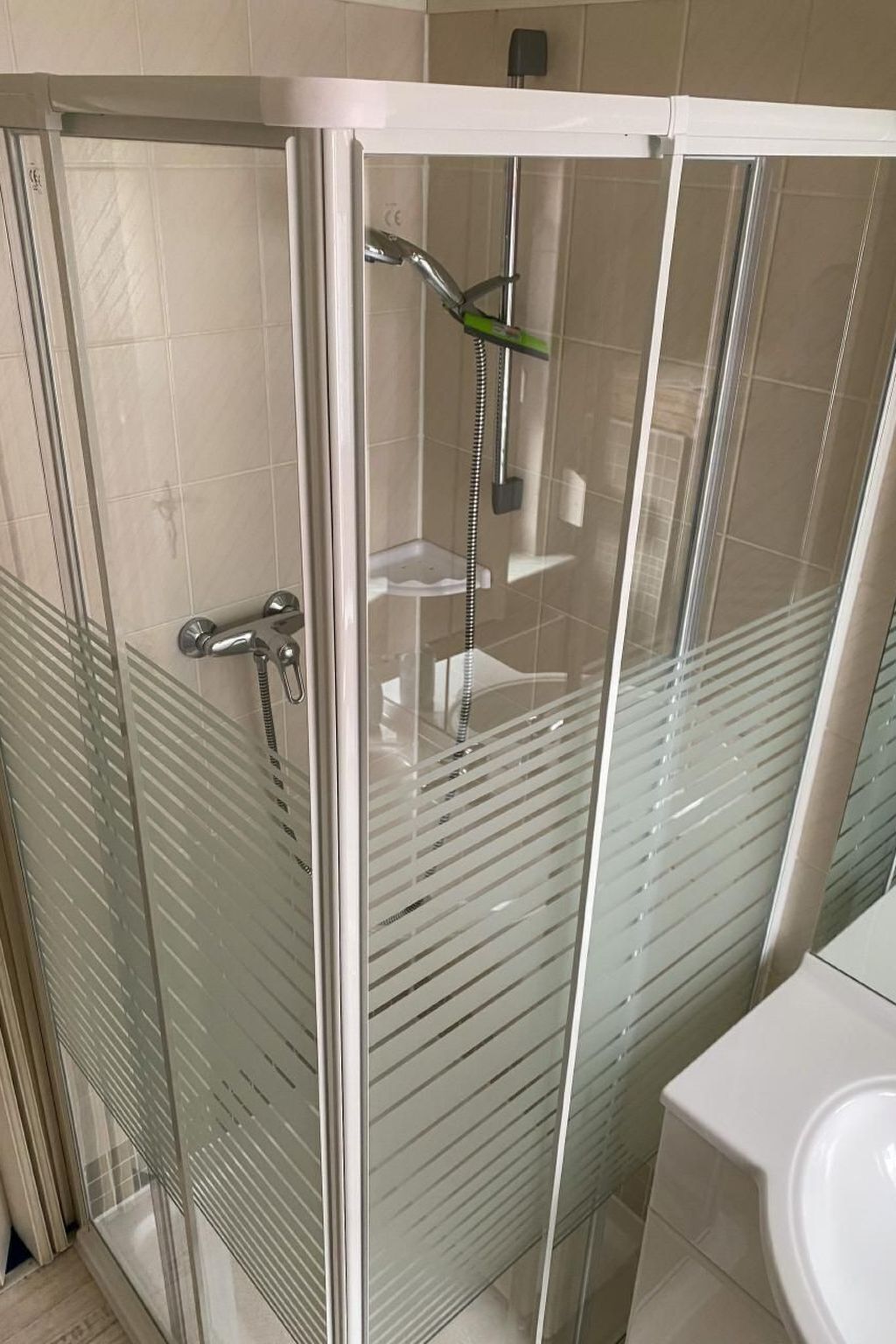 Une douche fermée par des parois en verre, dotée d’un pommeau de douche à main et d’un robinet fixé au mur.