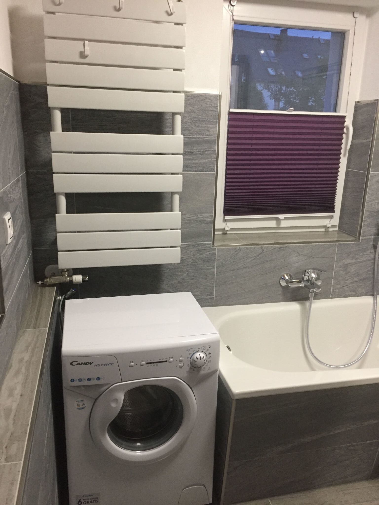 Ein modernes Badezimmer mit Waschmaschine, Badewanne und einem Fenster mit Jalousien.