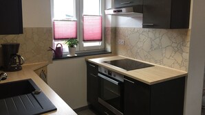 Une cuisine compacte équipée d’un four encastré, d’une machine à café et d’une fenêtre avec des stores.