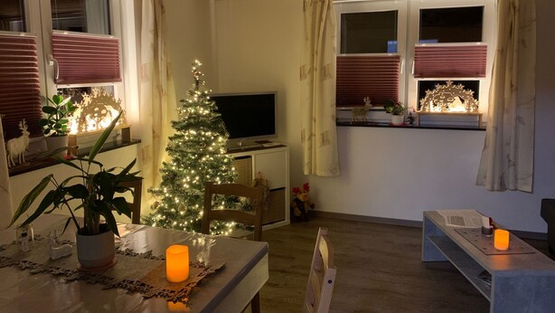 Un salon chaleureux avec un sapin de Noël, un téléviseur et un coin repas comprenant une table et des chaises.
